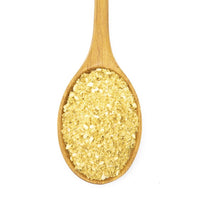 A wooden spoon with yellow, crumbly Korean BBQ Rub Seasoning—ideal for adding depth to meat dishes—is displayed against a white background.
