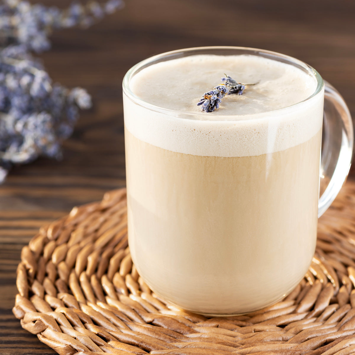 Glass mug of creamy beverage with lavender flowers on a wooden surface