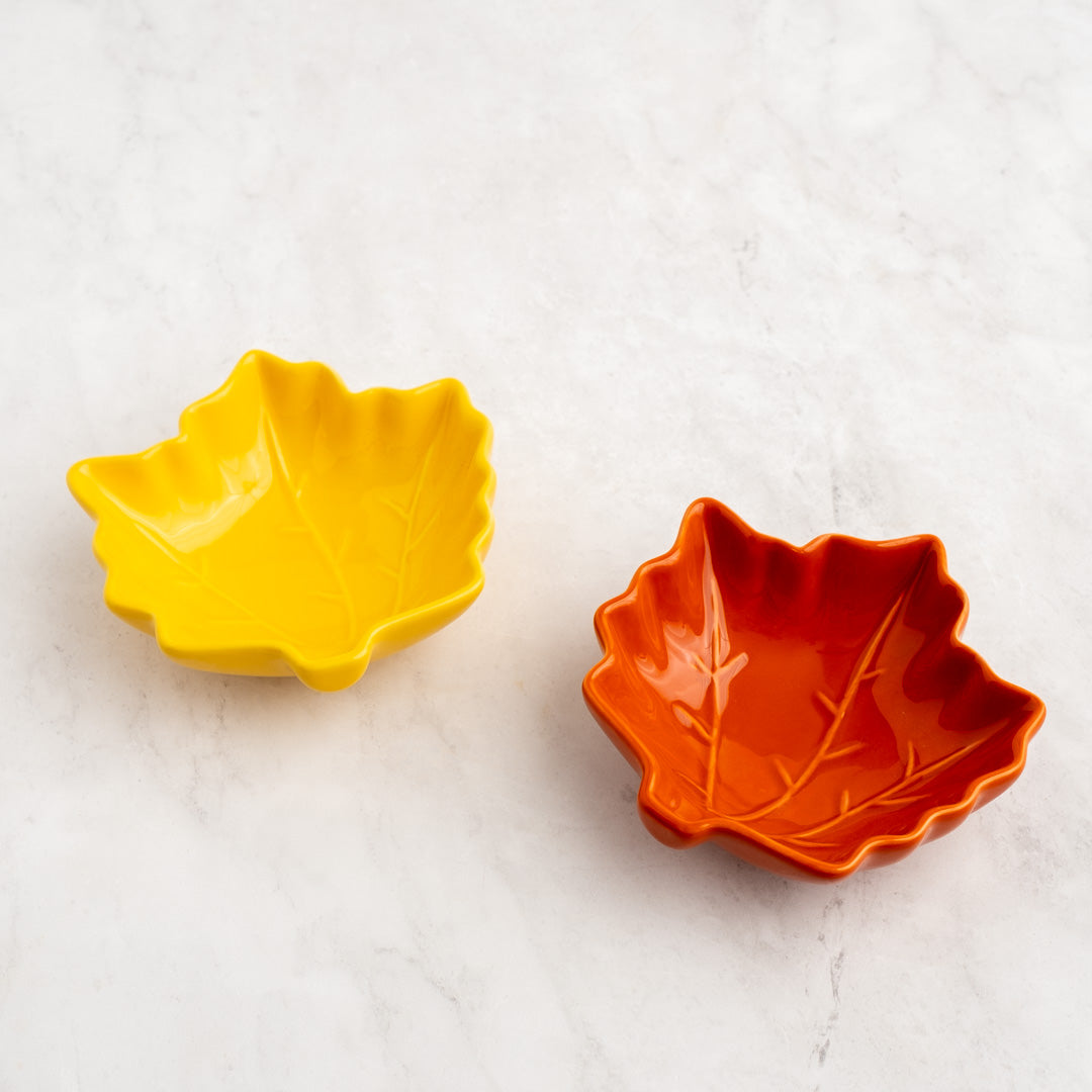 Two leaf-shaped bowls, one yellow and one orange, on a light gray background.