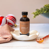 Bottle of vanilla extract on a decorative plate with festive ornaments in the background
