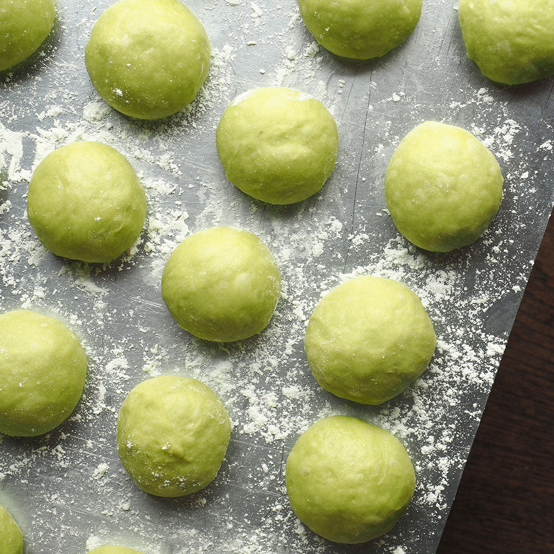 Green dough balls arranged on a flour-dusted baking sheet.