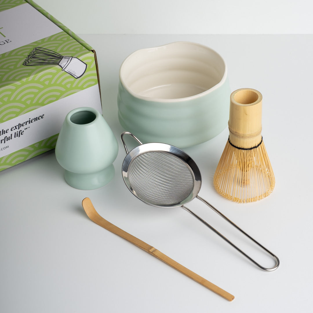 Tea-making tools including a Matcha Bowl (ceramic), Matcha Whisk (bamboo), Whisk Holder (ceramic), Matcha Sieve (stainless steel), Matcha Scoop (bamboo) on a white surface with a branded box.