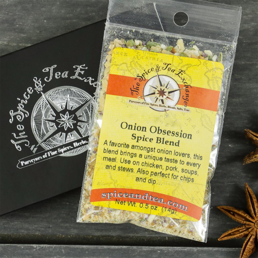 A packet of Onion Obsession Spice Blend - Barter Box rests on a dark wooden surface beside a black Spice & Tea Exchange box and star anise—an ideal gift for fans of onion seasoning.