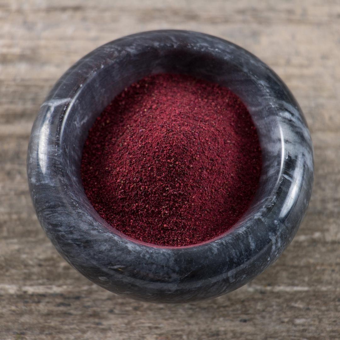 A black marble bowl filled with Organic Beet Root Powder sits on a wooden surface, highlighting its rich nutrients and natural dye qualities.