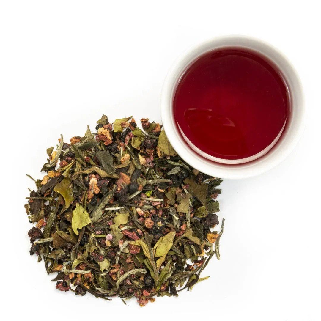 Berry White Tea, a loose leaf blend of green and brown leaves with real berry pieces, sits beside a white cup of bright reddish brew, all displayed on a clean white background.