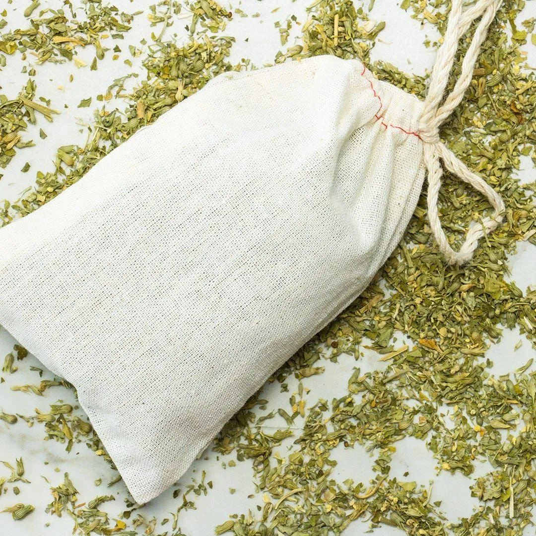 A white drawstring cloth bag of Organic Catnip lies slightly open on a surface scattered with dried catnip, creating an irresistible scene for your cat.