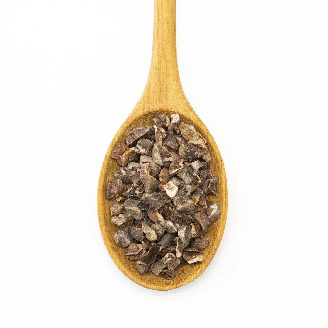 A wooden spoon holds dried, chopped Cocoa Nibs, displayed on a white background.