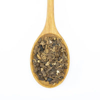 A wooden spoon holds small, chopped Dandelion Root - Roasted, a popular coffee alternative, displayed against a white background.
