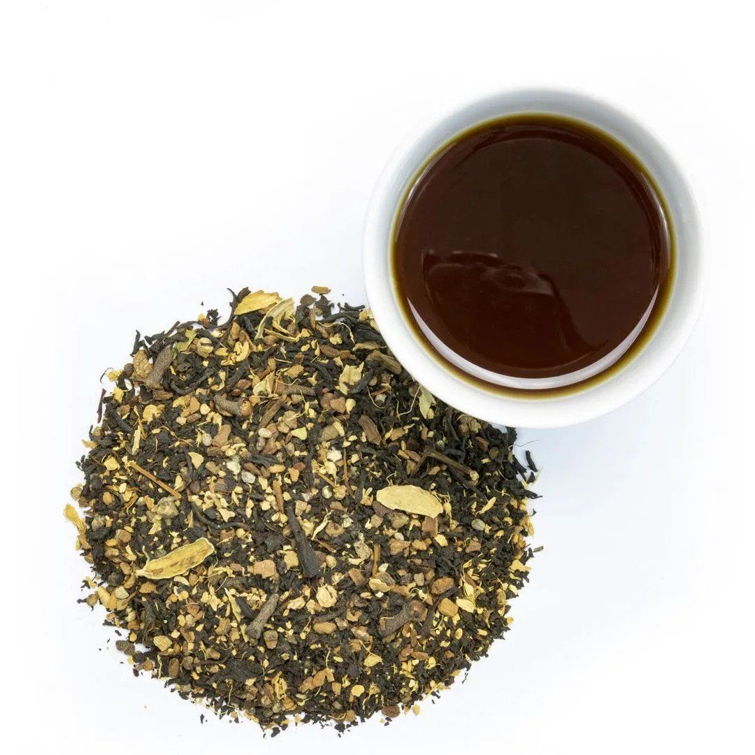 Emperor's Chai Tea loose-leaf blend, with visible masala spices and cinnamon, is shown next to a white cup filled with rich, dark brown brewed tea on a white background.