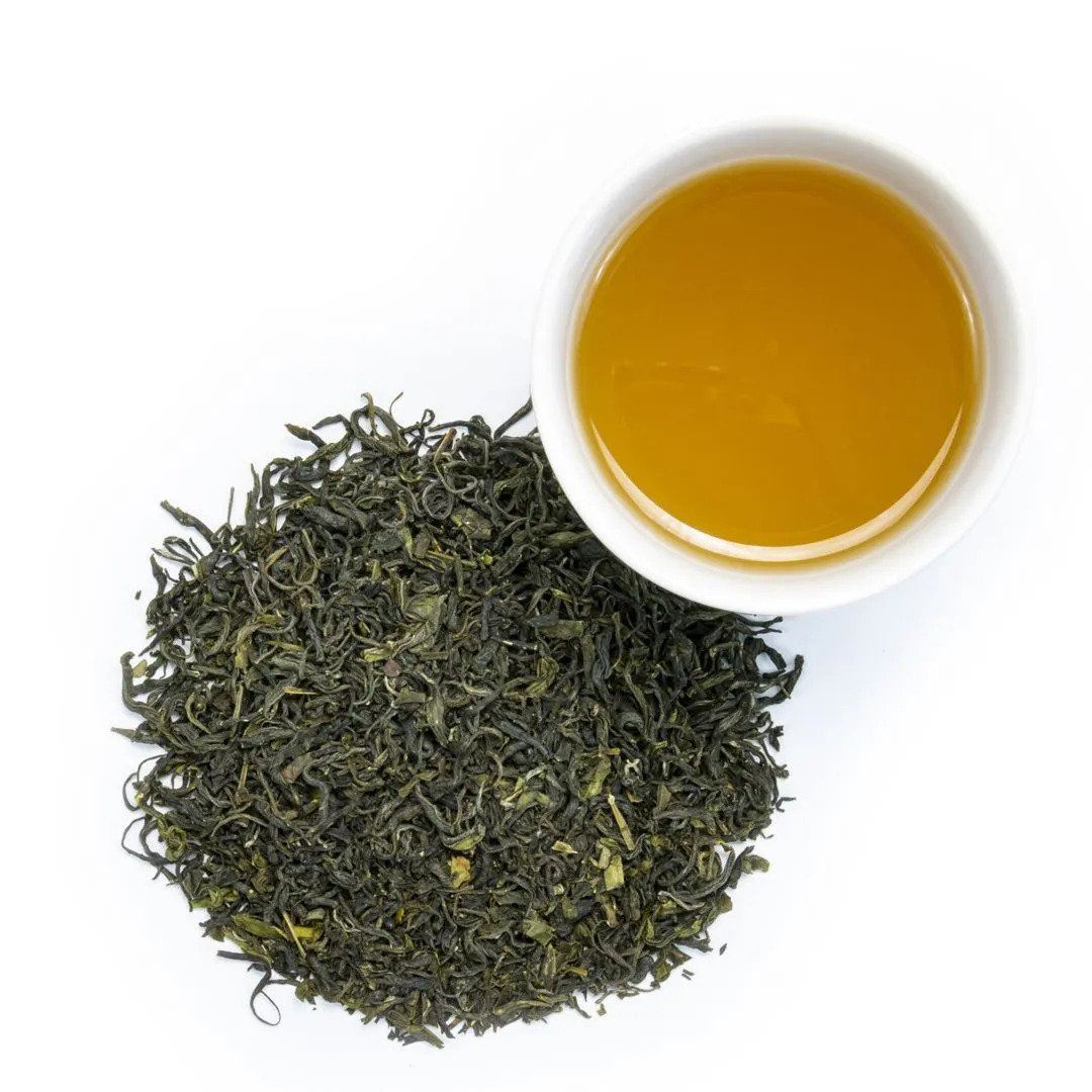 A pile of Jade Cloud Tea from Hubei, China sits beside a white cup filled with golden brewed tea, all set against a white background.