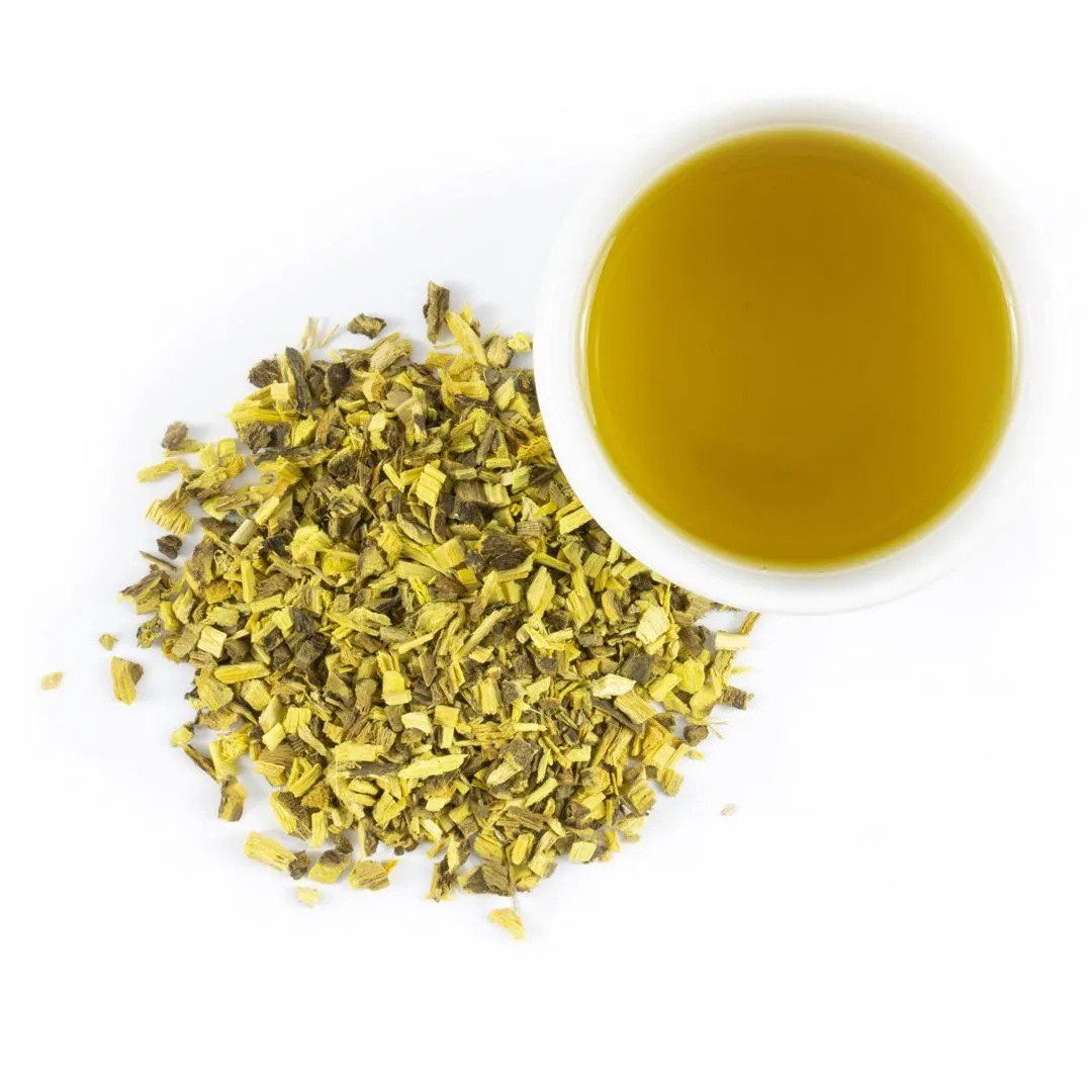 A white cup of yellow-green tea brewed from Licorice Root - Cut & Sifted, known for aiding digestion, sits beside a small pile of dried herbal pieces on a white background.