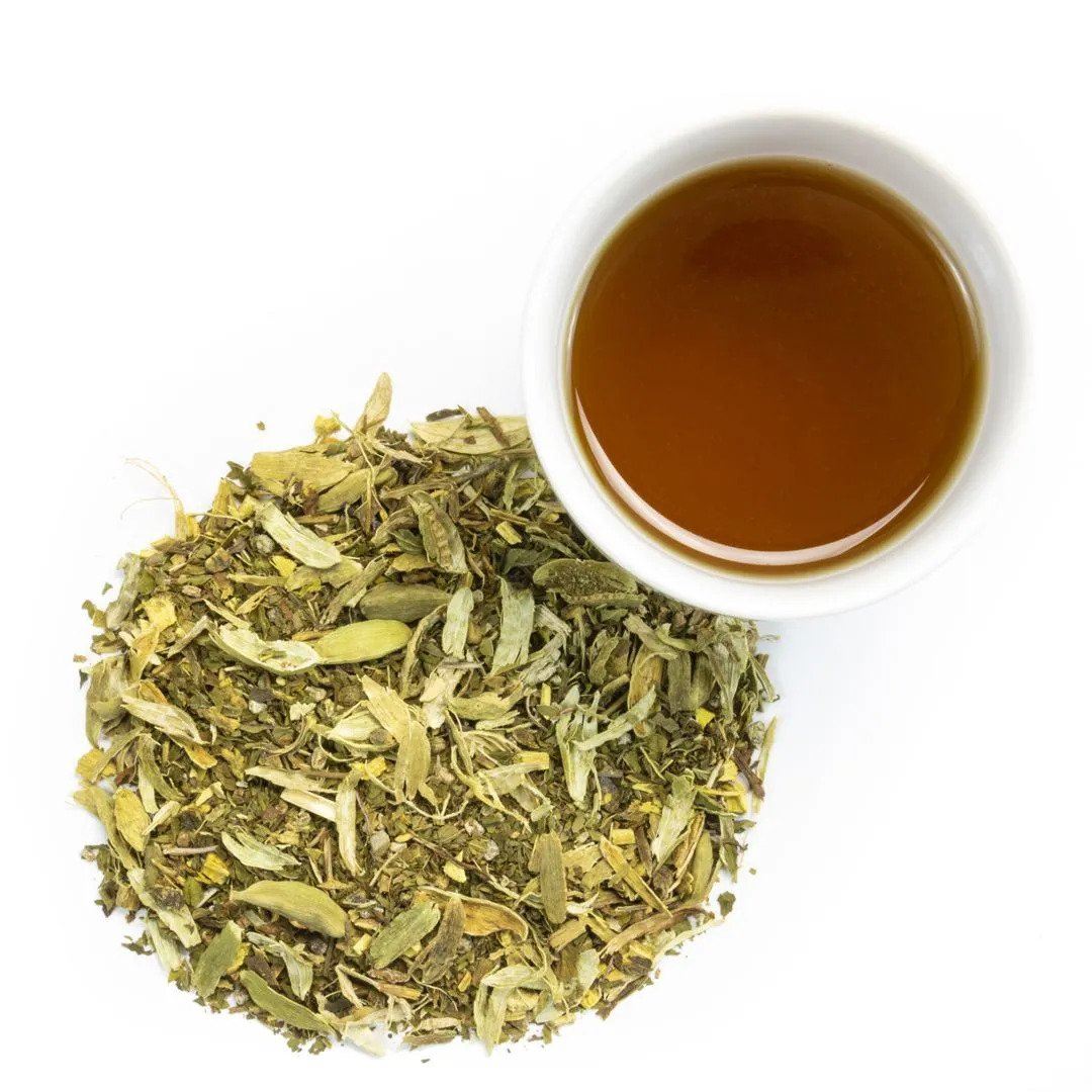 A cup of Mint Basil Herbal Tea sits beside loose, dried leaves and seeds on a white background, offering a refreshing herbal tea experience.