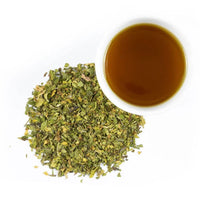 A cup of brown tea, highlighted by Organic Peppermint, sits on a white background beside a loose pile of dried green tea leaves for a refreshing touch.