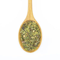 A wooden spoon filled with Organic Peppermint and other dried green herbs, photographed on a white background.