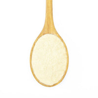 A wooden spoon holds fine, light-colored Organic Peruvian Maca Powder, a renowned adaptogen, displayed on a white background.