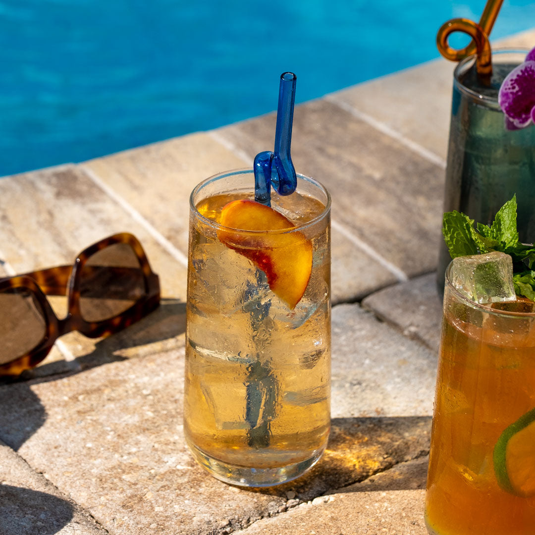 Peach Blossom Herbal Tea brewed and served over ice with a peach garnish in a glass poolside