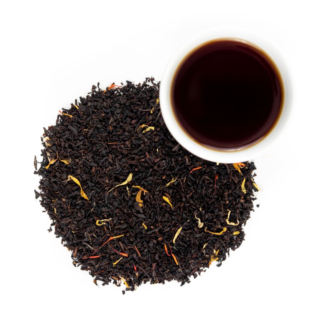 A cup of Peach On The Beach Tea rests atop a pile of black tea leaves, offering a fruity and soothing moment to unwind.