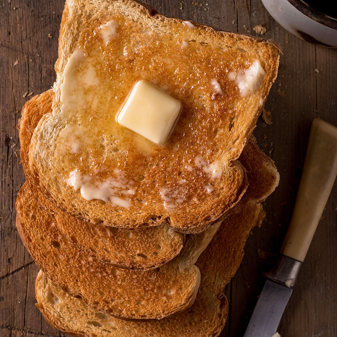 Stack of buttered toast on a wooden surface with a knife and cup of coffee.