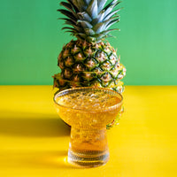 Pineapple Paradise Green Tea iced in a glass next to a sliced pineapple