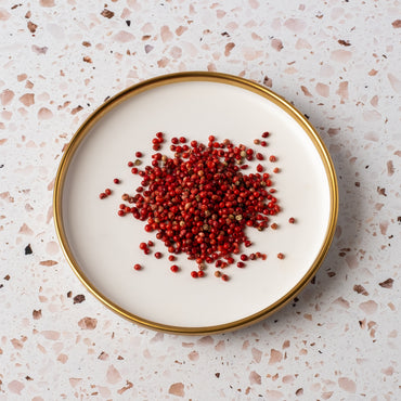 A round plate with a gold rim holds a pile of Pink Pepperberry, set on a pink and white terrazzo surface.