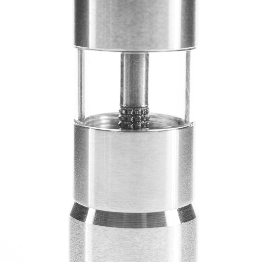 A close-up of the Pump & Grind Salt & Pepper Mill, a compact stainless steel cylinder with a transparent section displaying ball bearings around a central rod, photographed against a white background.
