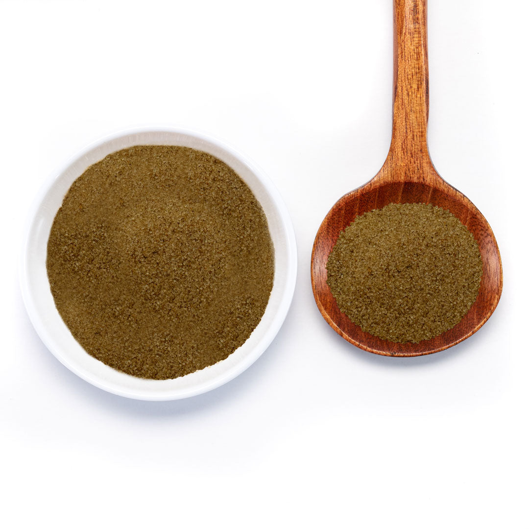A white bowl and a wooden spoon, both filled with Pumpkin Spice Monk Fruit Sweetener, a fine brown natural sweetener, are set against a white background.