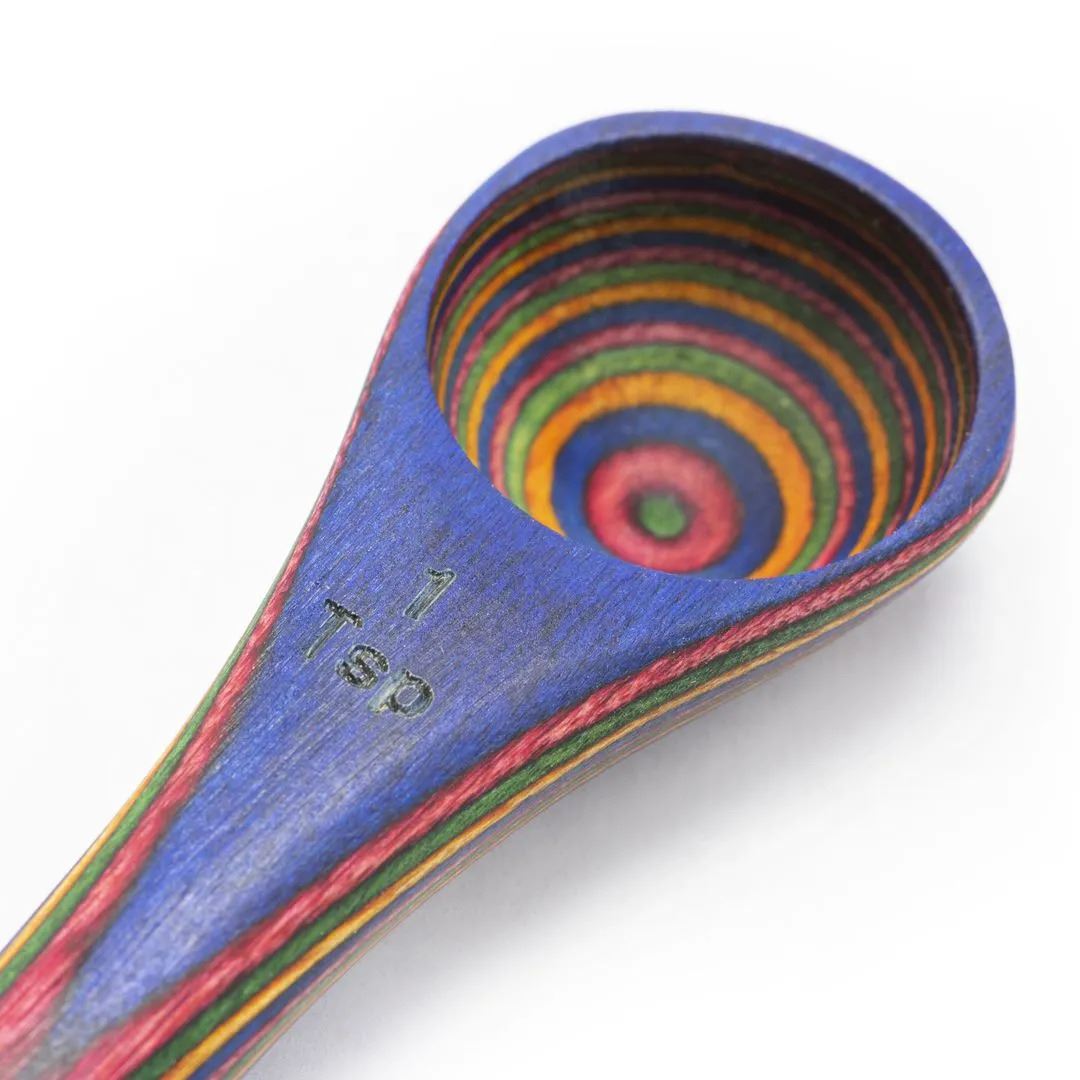A close-up of the Rainbow Double Ended Spoon, crafted from laminated Pakkawood, features vibrant concentric circles in red, yellow, green, and blue on both the interior and handle, with a 1 tsp marking.