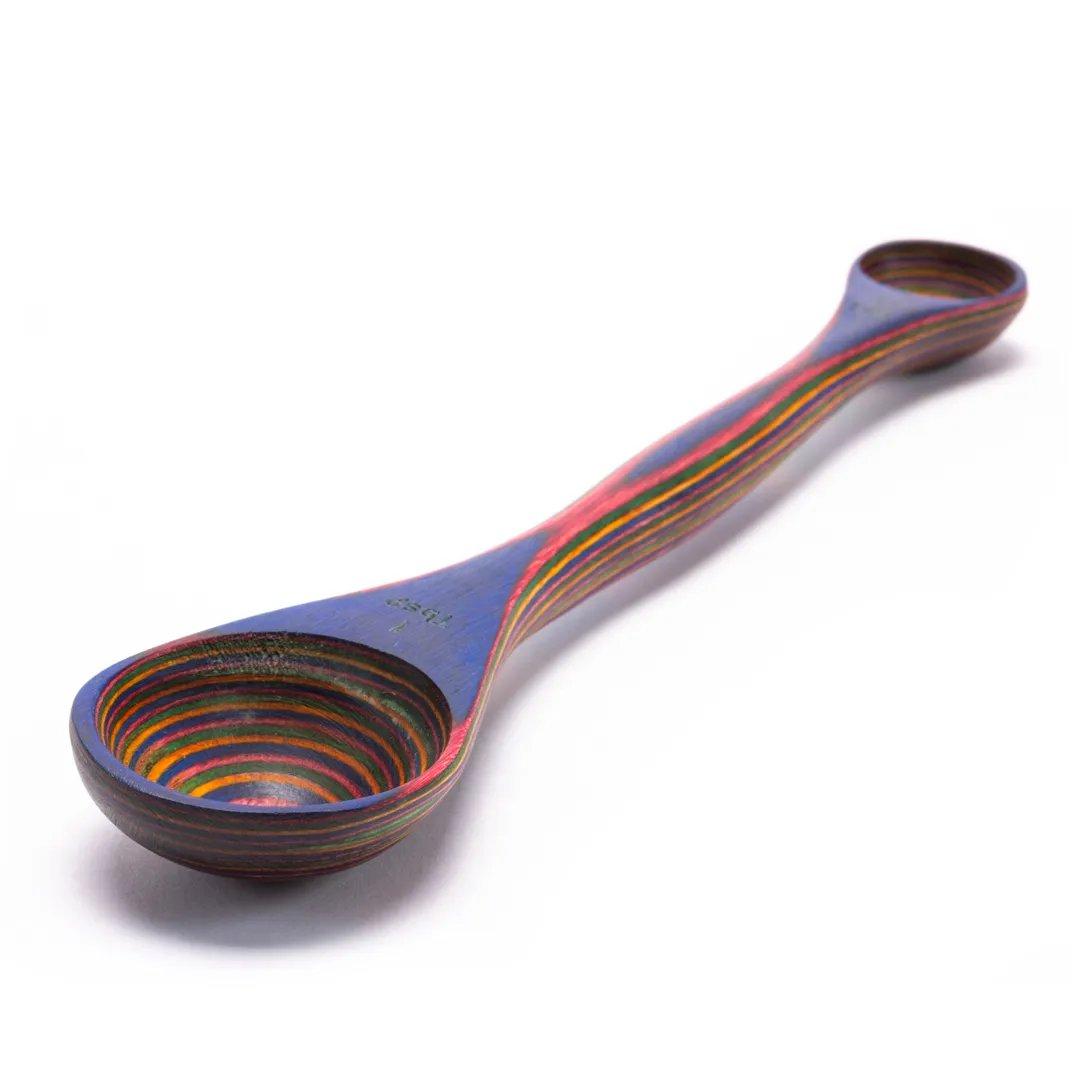 The Rainbow Double Ended Spoon is crafted from eco-friendly laminated Pakkawood, featuring vibrant concentric rings and large and small measuring spoons on each end.