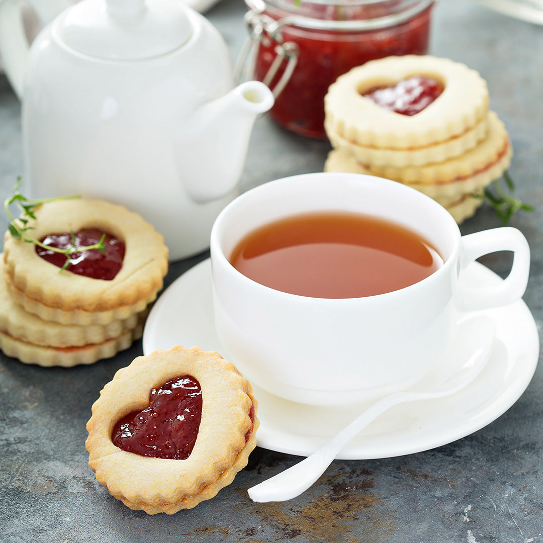 White teacup with tea, cookies with jam, and a teapot on a gray surface