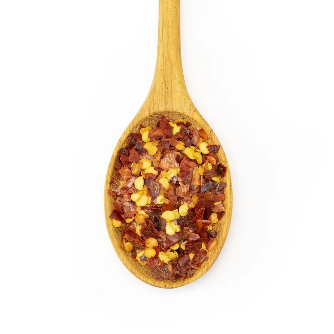 A wooden spoon holds Crushed Red Pepper Flake, made from dried chile peppers like cayenne, displayed on a white background.
