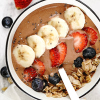 Chocolate smoothie bowl with bananas, strawberries, and blueberries in a white bowl.