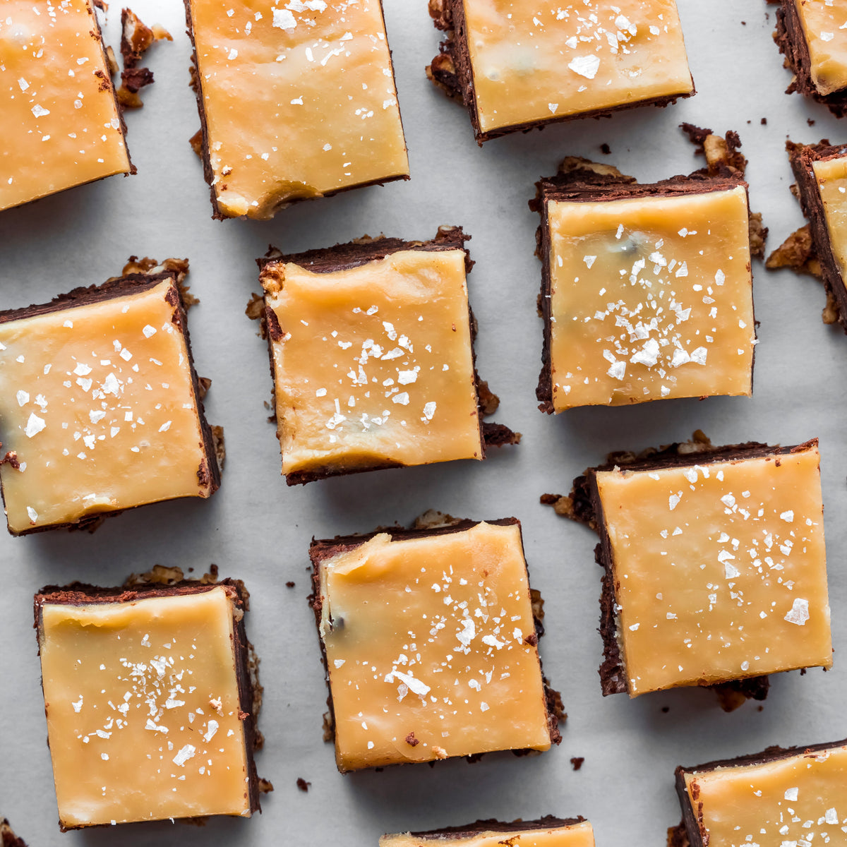 Square brownies with caramel topping and sea salt on a light gray background