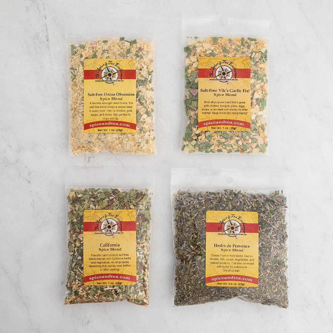 The Salt-Free Blends Sampler features four clear spice packets with colorful labels, arranged in a square on light marble, containing onion, garlic, California mix, and herbs de Provence spice blends.