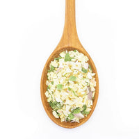 A wooden spoon holds Salt-Free Onion Obsession Spice Blend, a salt-free mix of dried green, white, and light-yellow vegetables perfect for dips and spreads, shown on a white background.