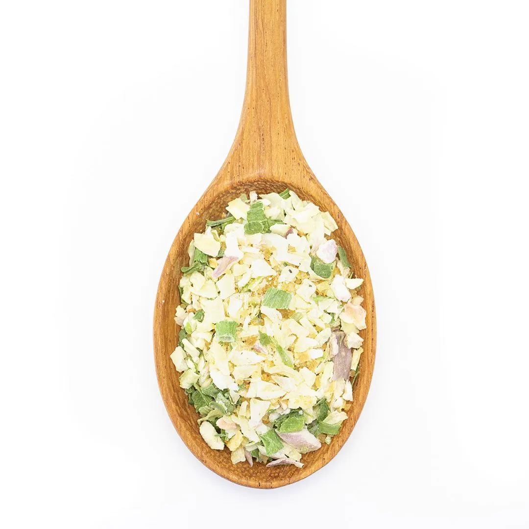 A wooden spoon holds Salt-Free Onion Obsession Spice Blend, a salt-free mix of dried green, white, and light-yellow vegetables perfect for dips and spreads, shown on a white background.