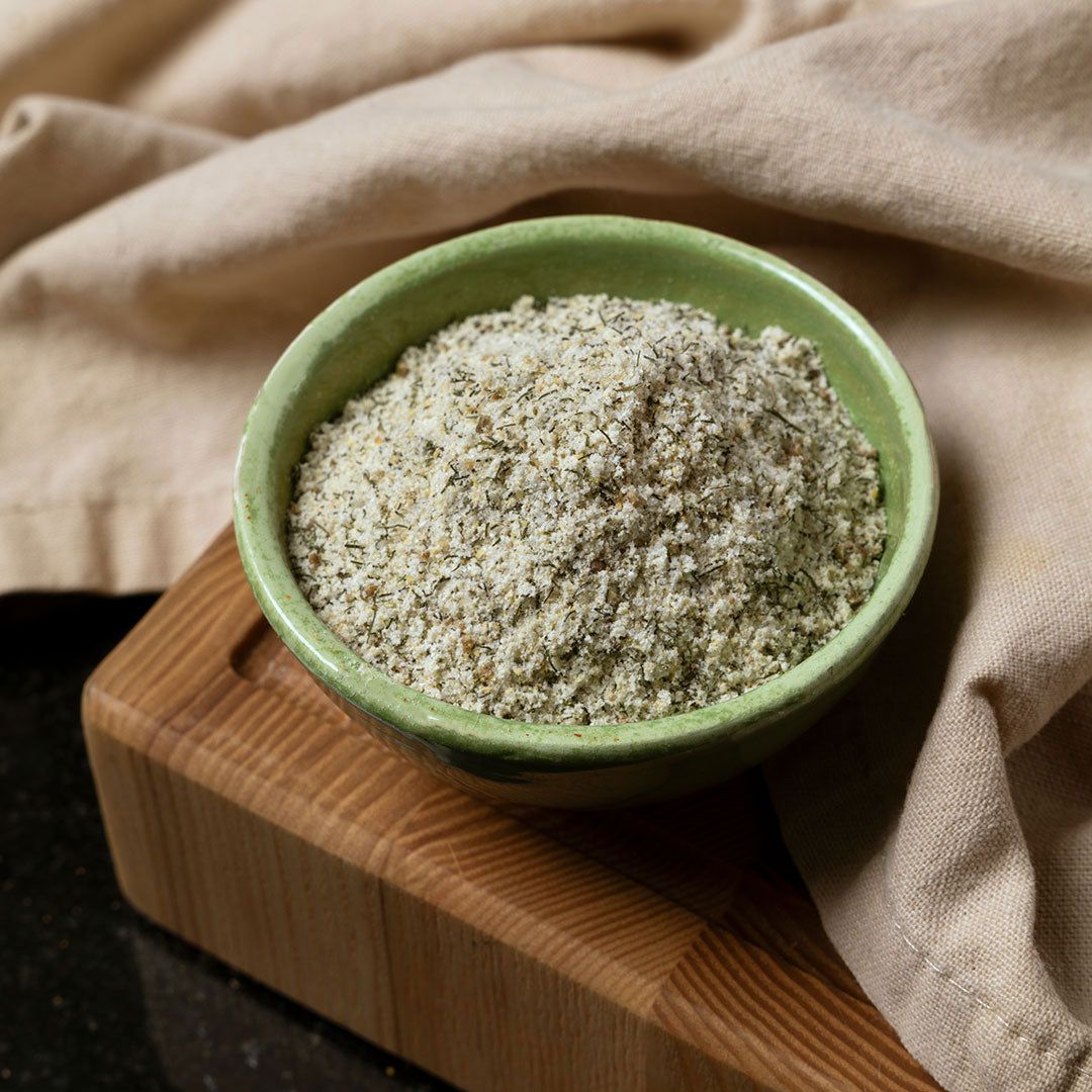 A small green bowl filled with French Fry Seasoning - Salt 'n Vinegar sits on a wooden cutting board, with a beige cloth in the background.