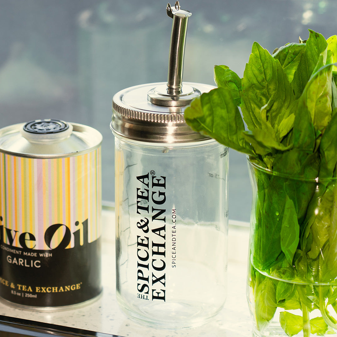 Shake, Strain, and Pour Jar - can of olive oil, and bunch of green basil leaves on a light surface.
