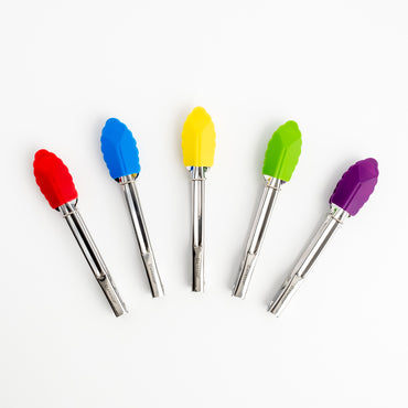 Five Mini Tongs with colorful silicone tips—red, blue, yellow, green, and purple—are fanned out on a white background. These stainless steel Mini Tongs bring a playful and practical touch to any kitchen.