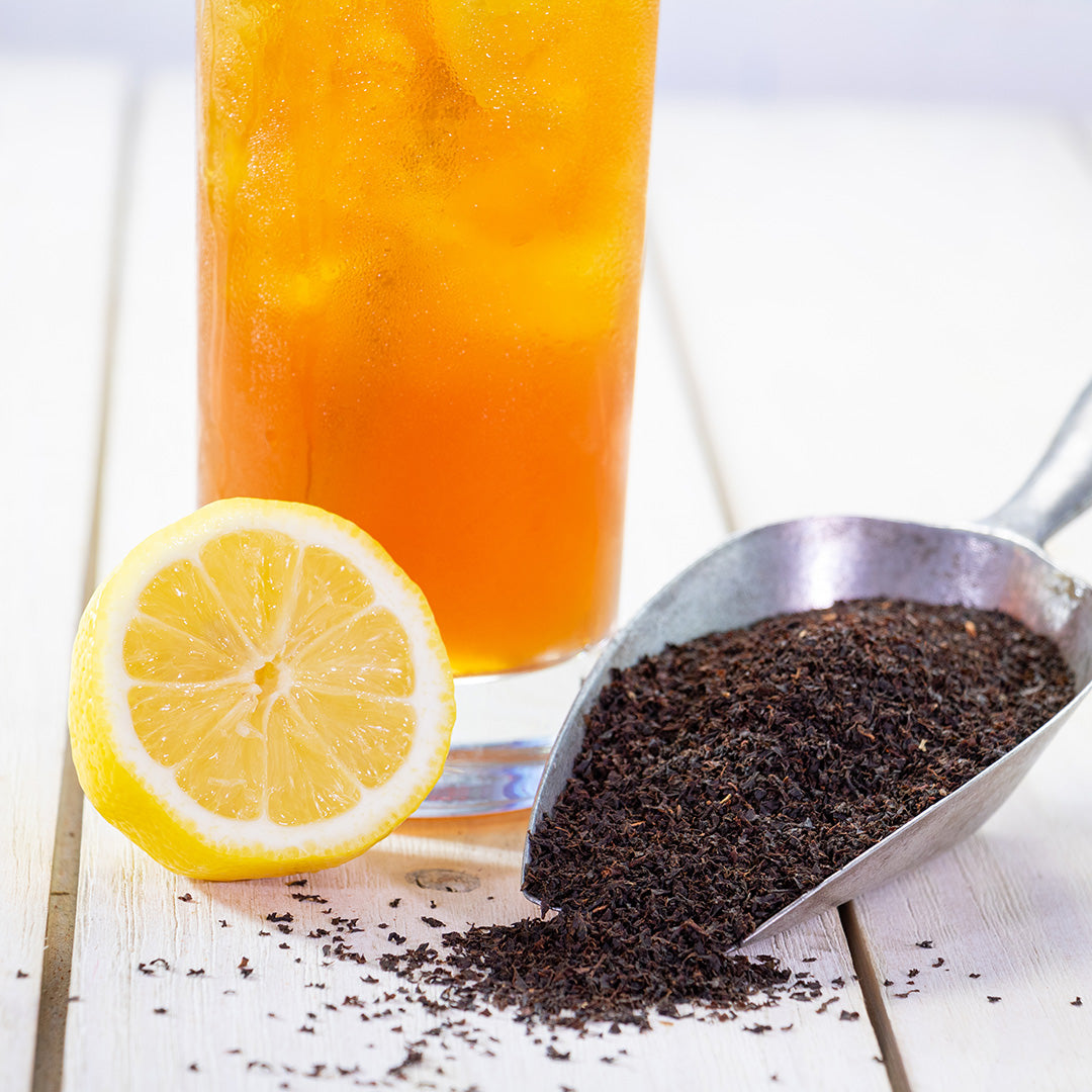 Southern Iced Tea served with lemon slices, a half-cut lemon, and a metal scoop of loose black tea leaves on a white wooden surface highlights its traditional flavor.