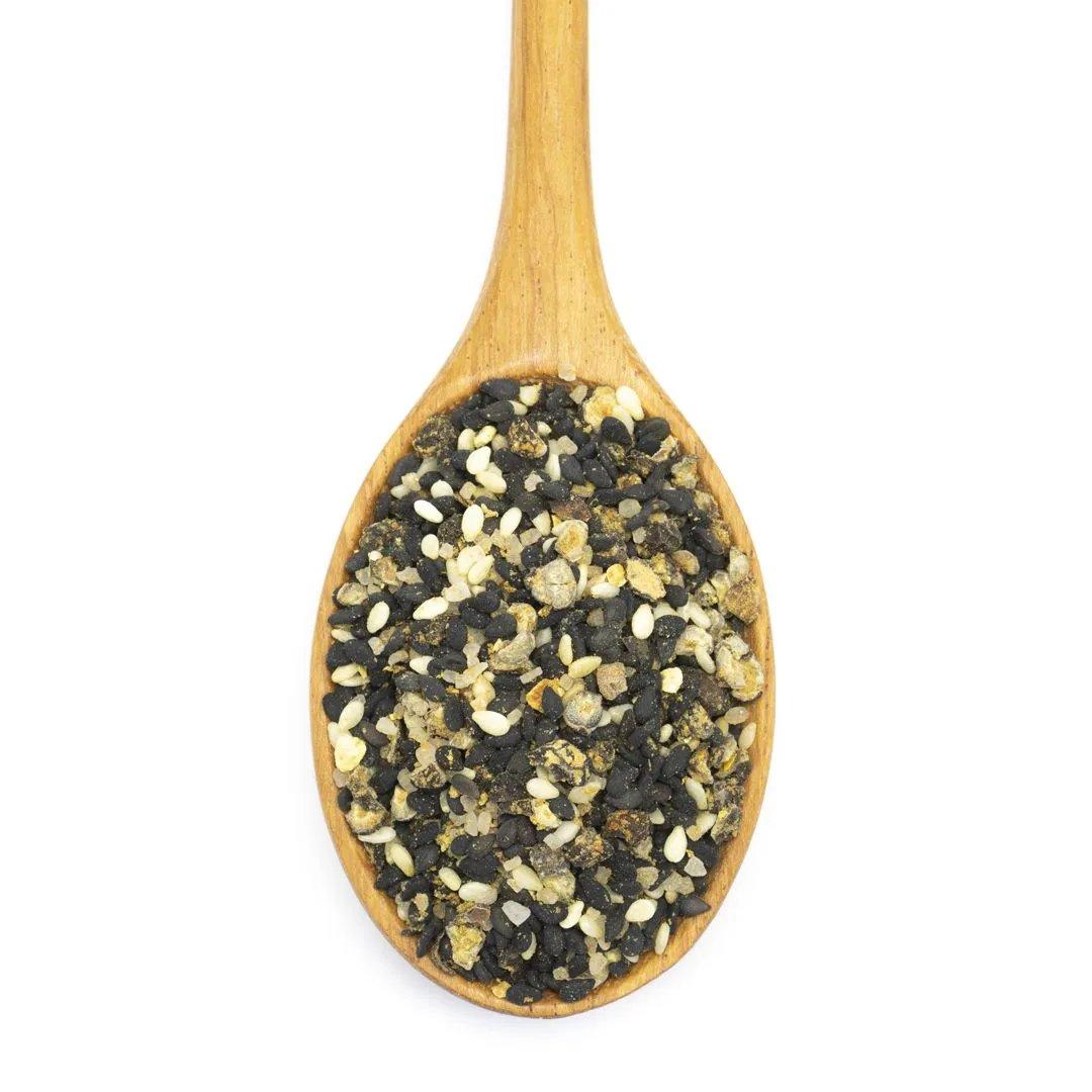 A wooden spoon filled with Spicy Tuna Rub Seasoning—a blend of black and white sesame seeds, spices, and Japanese flavors—isolated on a white background.