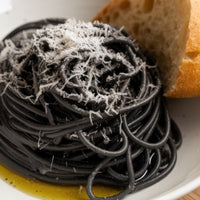 Black spaghetti with grated cheese on a white plate with bread
