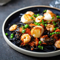 Plated dish of black spaghetti with seafood and peas on a dark surface