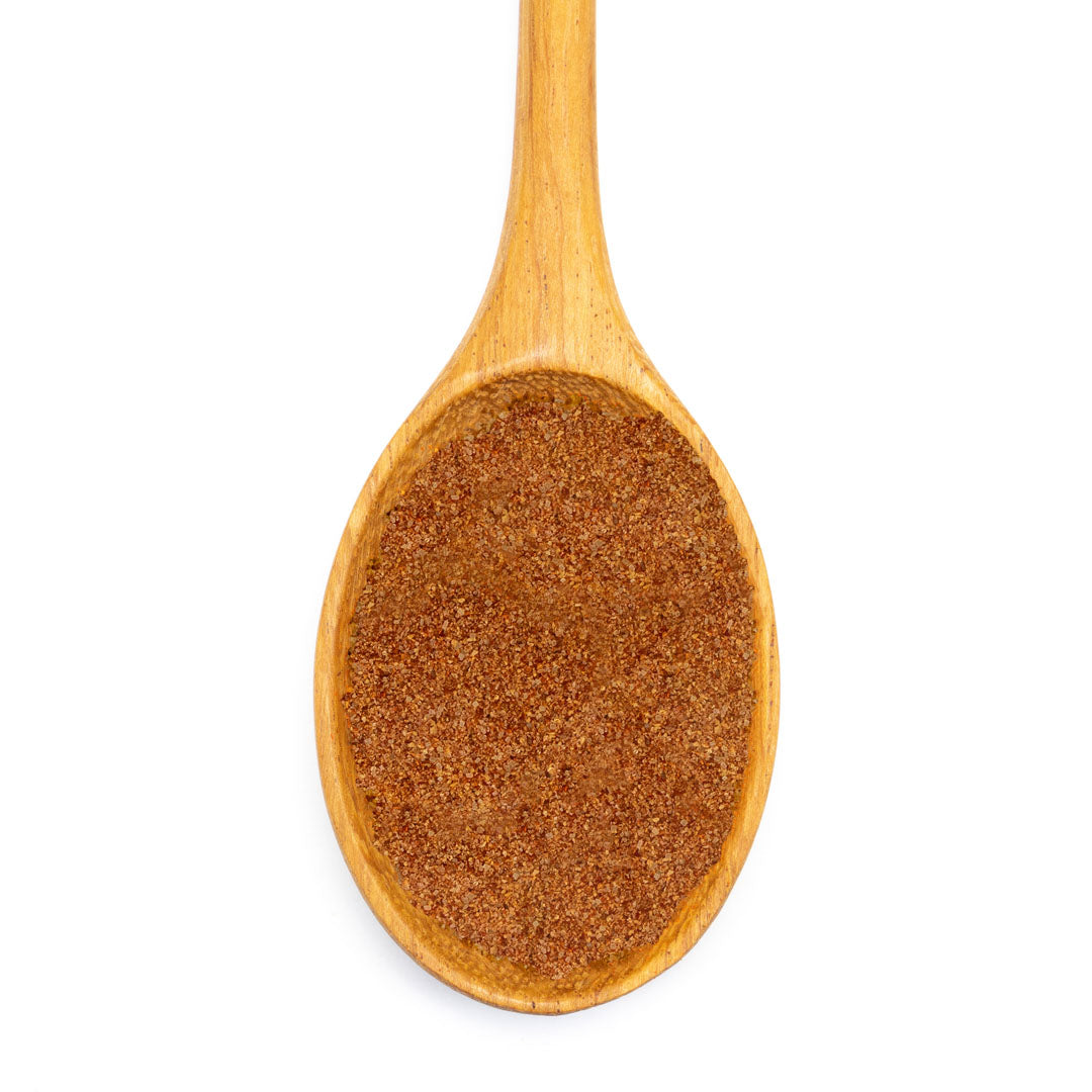 A wooden spoon filled with French Fry Seasoning - Sweet 'n Smoky, a fine, reddish-brown blend, viewed from above on a white background.