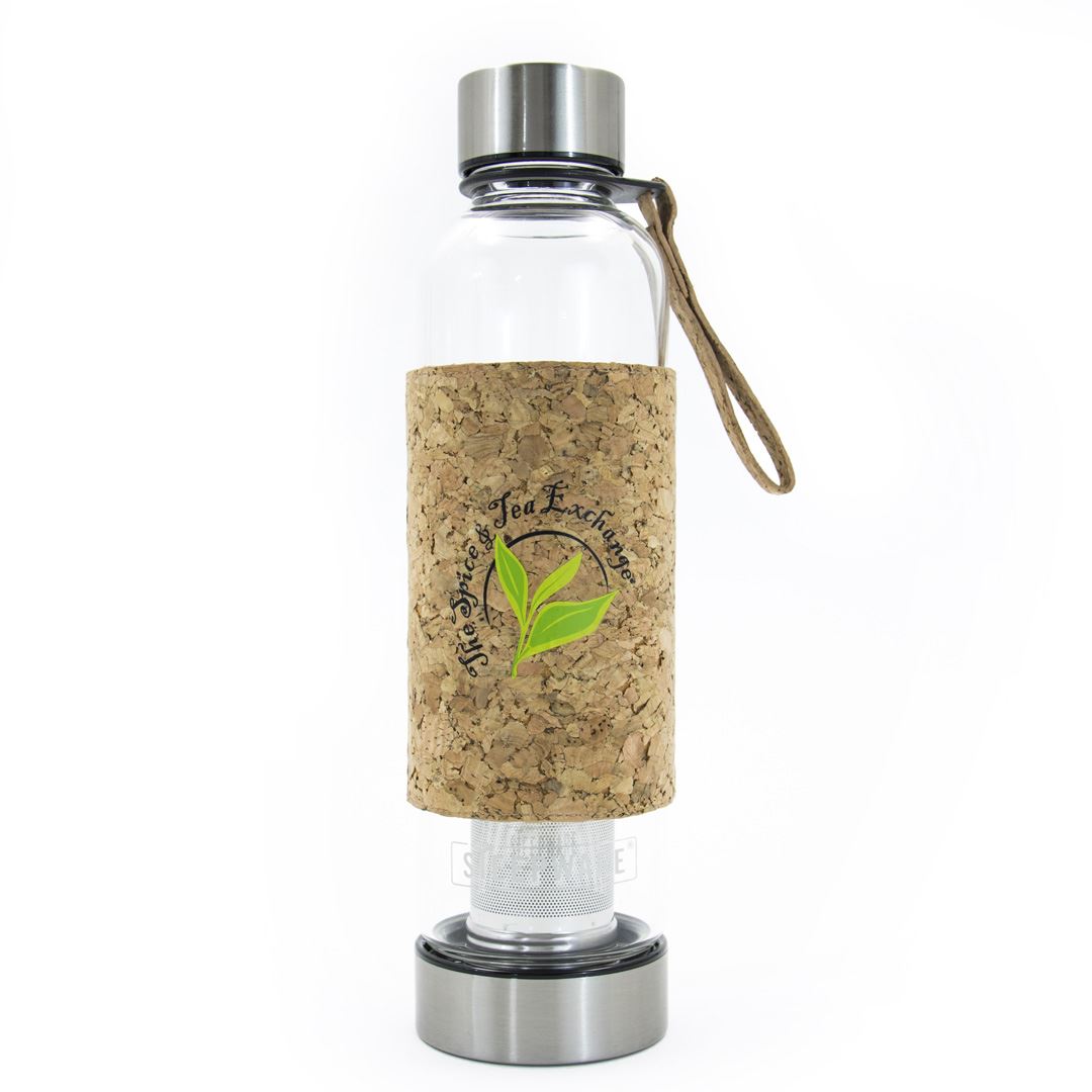 The Urban Tea Tumbler is a clear glass bottle with a metal lid and base, cork sleeve displaying a green leaf logo and The Herbal Tea Exchange text. Eco-friendly, with a brown strap attached to the lid for easy carrying.