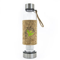 The Urban Tea Tumbler is a clear glass bottle with a metal lid and base, cork sleeve displaying a green leaf logo and The Herbal Tea Exchange text. Eco-friendly, with a brown strap attached to the lid for easy carrying.
