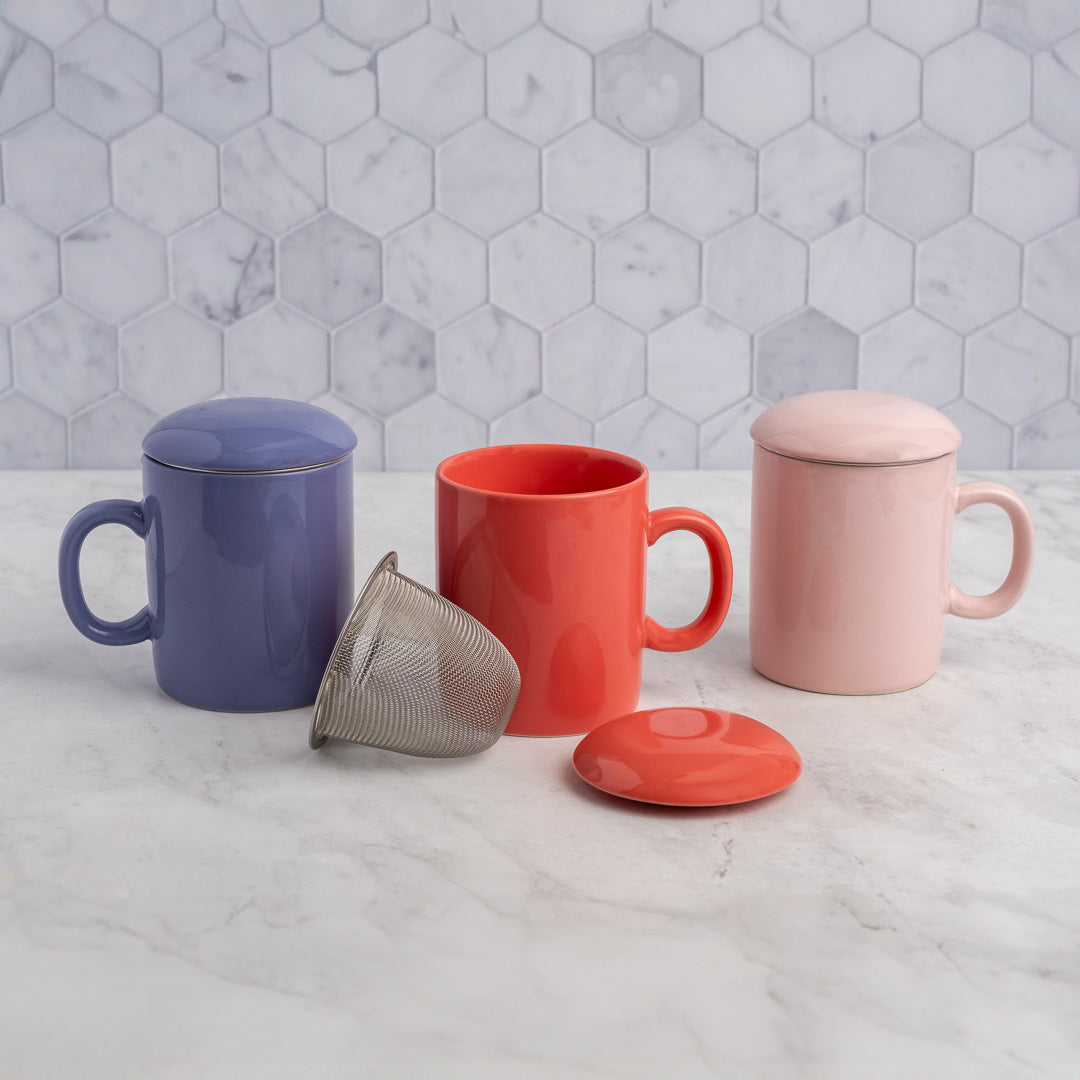 Three mugs in blue, red, and pink with various lids on a marble surface.