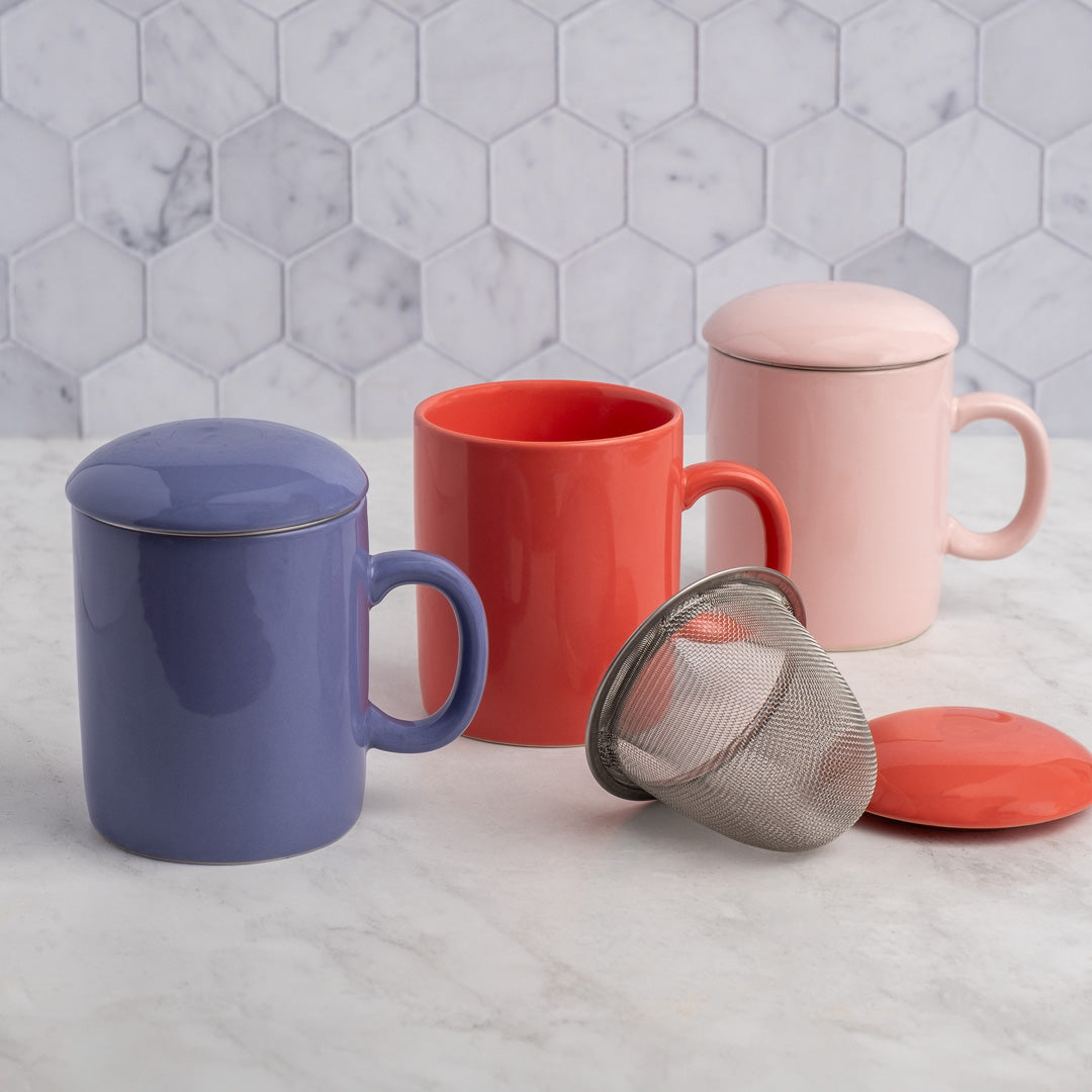 Set of colorful mugs with lids and a strainer on a marble surface.