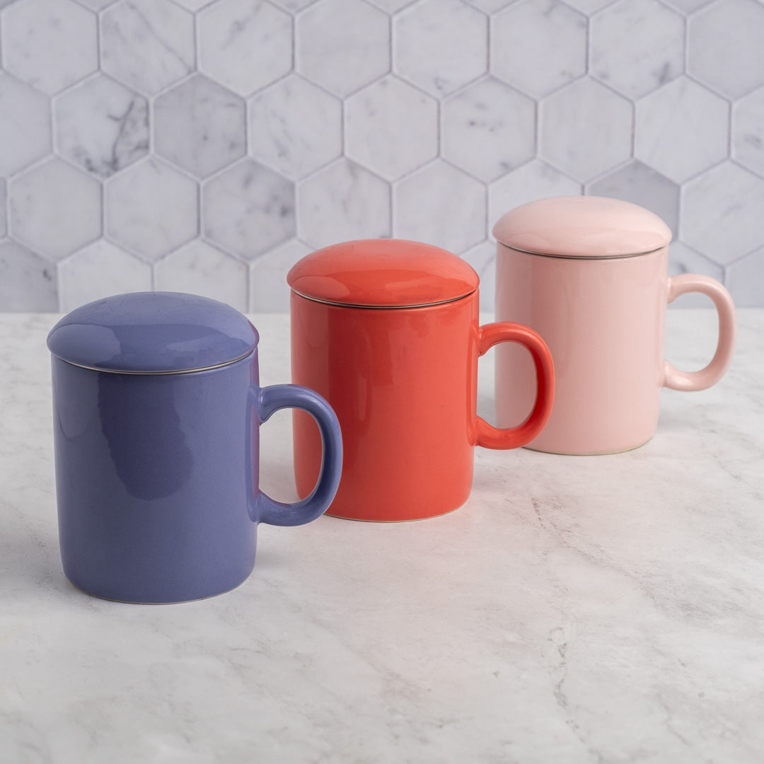 Three colorful mugs with lids on a marble surface with a hexagonal tile backsplash.