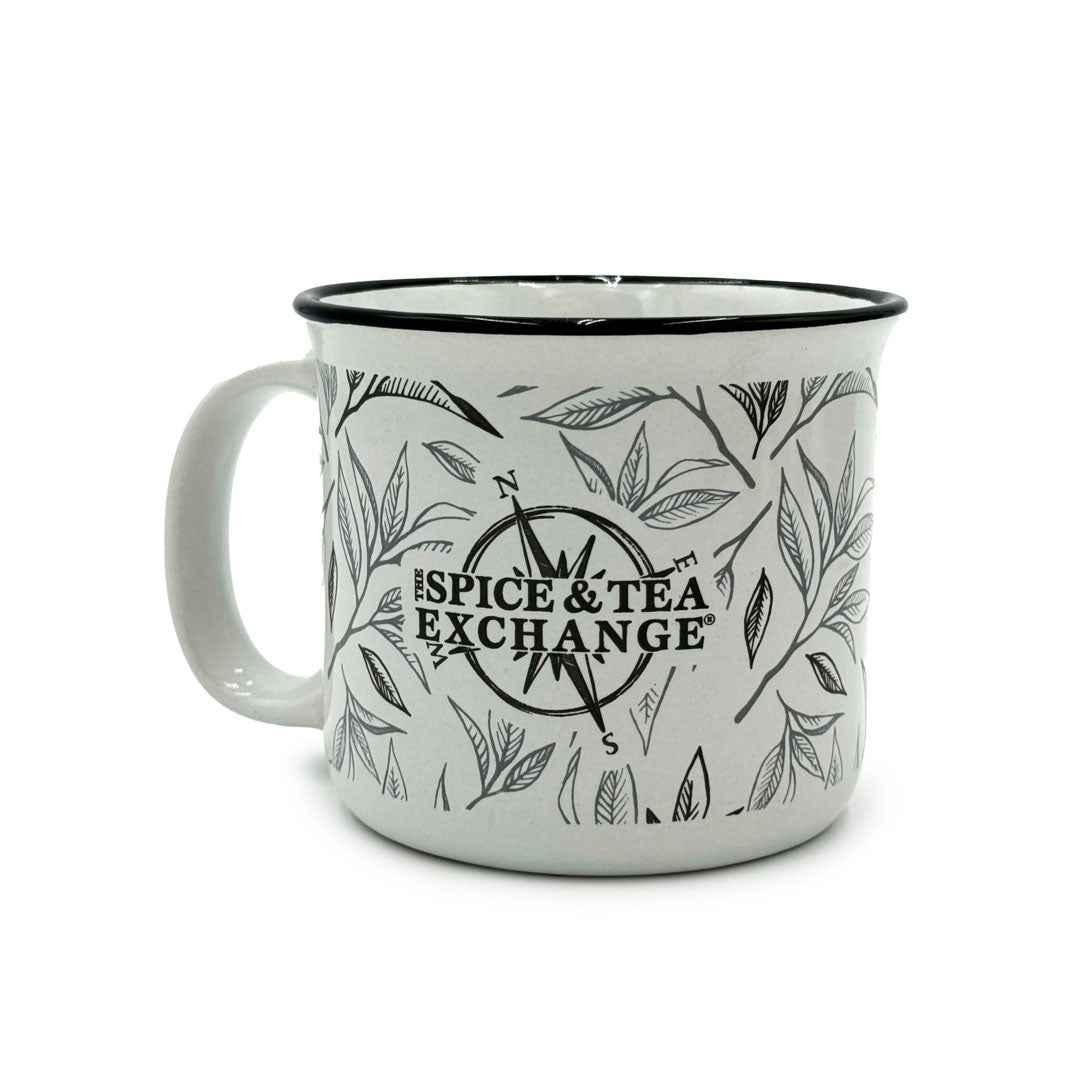The Tea Leaf Ceramic Camp Mug is a 12-ounce white ceramic mug with a black rim, decorated with a tea leaf motif and featuring a compass design and bold black "Spice & Tea Exchange" lettering on the front.