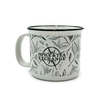 The Tea Leaf Ceramic Camp Mug is a 12-ounce white ceramic mug with a black rim, decorated with a tea leaf motif and featuring a compass design and bold black "Spice & Tea Exchange" lettering on the front.